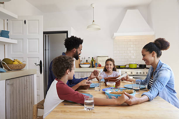 Family hold hands around the kitchen table before their meal Family hold hands around the kitchen table before their meal saying grace stock pictures, royalty-free photos & images