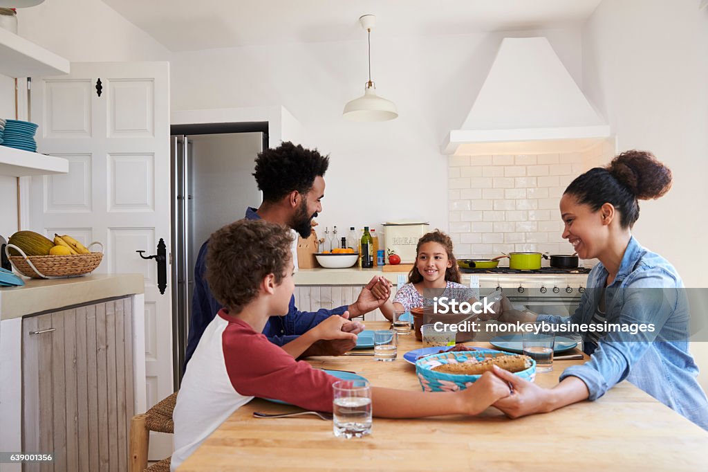 Família de mãos dadas em torno da mesa da cozinha antes de sua refeição - Foto de stock de Família royalty-free