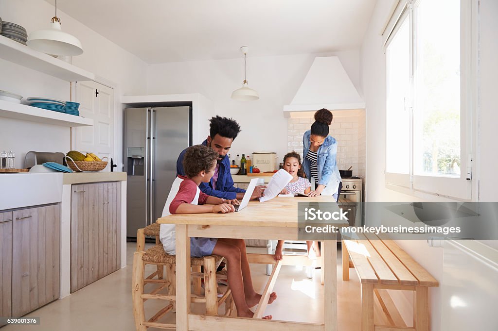 Mum and dad help their kids with homework at kitchen Mum and dad help their kids with homework at kitchen table Family Stock Photo
