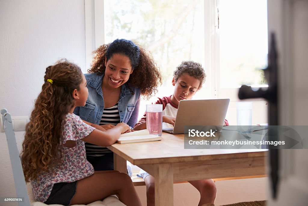 Mum sitting with kids at kitchen table, son using laptop Child Stock Photo