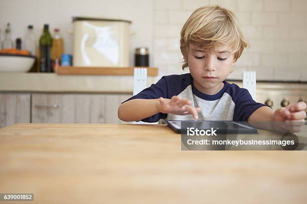 Niño Usando La Tableta En La Mesa De La Cocina Vista Frontal Foto de stock y más banco de imágenes de Niño