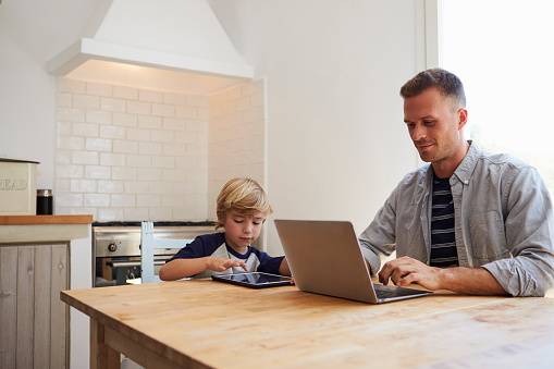 Father and son using computers at the kitchen table