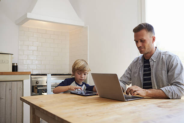 father and son using computers at the kitchen table - child looking blank offspring imagens e fotografias de stock