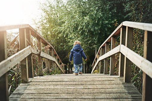 Little girl dressed in warm clothes jumping from wooden table with beautiful lake in background. Out to enjoy nature, relaxing while the beautiful scenery surrounds the place. scenery surrounds the place.