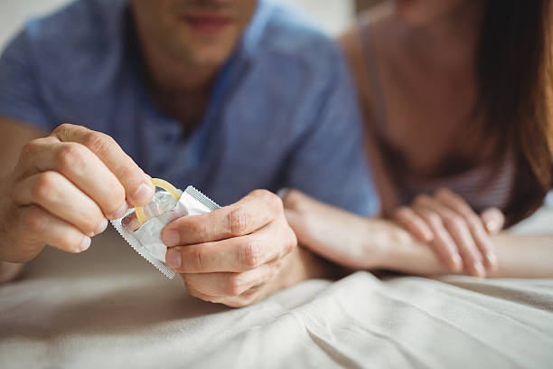 gros plan du couple avec un préservatif au lit - condom photos et images de collection