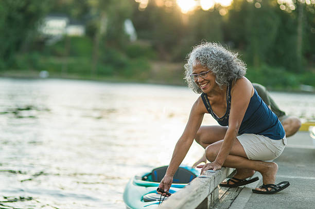 Older mature couple putting kayak in the water together Older mature couple putting kayak in the water together before heading out on the water active seniors summer stock pictures, royalty-free photos & images