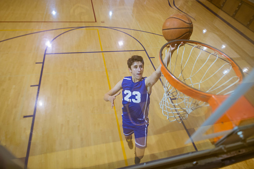 A male high school basketball player rises to the hoop for a driving lay-in