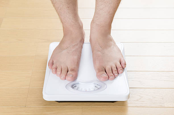 istock Foot of man standing on bathroom scale 639031120