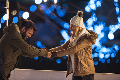 Happy couple holding hands while ice skating together.