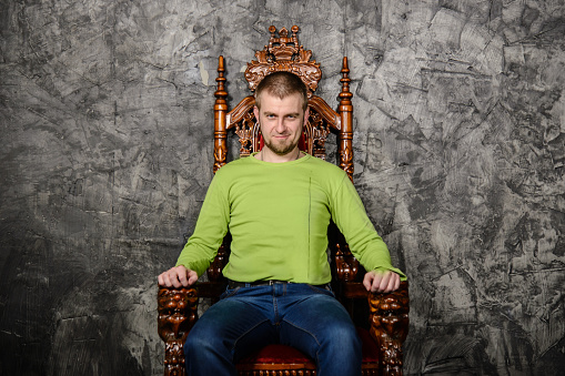 Attractive young man in a light green t-shirt sitting on the throne and smiling looking at the camera