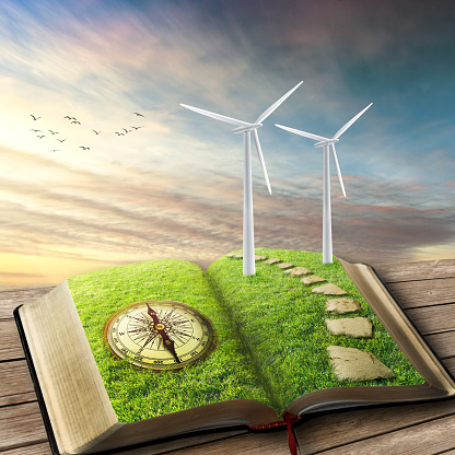 Renewable source of energy concept. Wind Generators, Ecology. Future of energy industry concept. Opened book covered with green grass compass and wind turbines installed with beautiful sky background