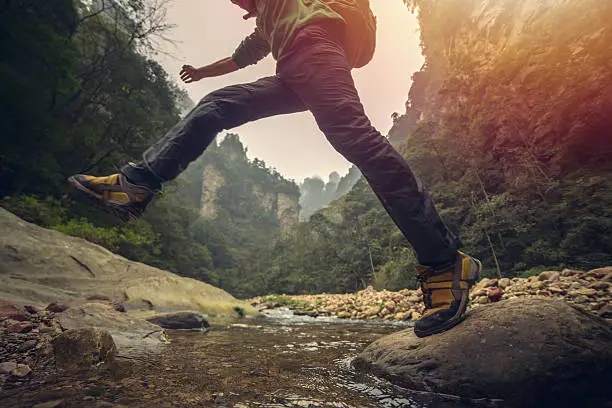 Young man hiking jumps over the mountain river. Low angle view, shot in Autumn in China.