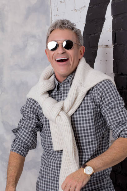 Man laughing in shirt with pullover on shoulders in dark glasses stock photo