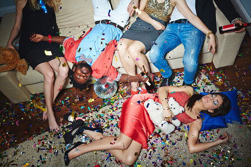 Tired friends sleeping on the floor and on couch with confetti