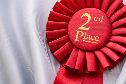 Close up view of Award Ribbon with golden sign for Second Place of real red fabric over white silk background