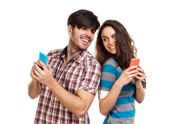Couple with cell phones Studio shot of boy and girl holding smart phones and looking back. man looking at phone over shoulder stock pictures, royalty-free photos & images