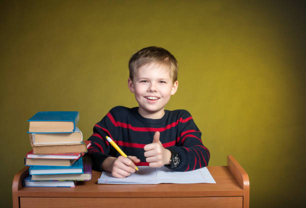 istock Happy kid doing homework with thumb up, books on table. 639100488