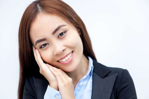 Close-up of face of young cheerful Asian businesswoman touching her face looking at camera and smiling