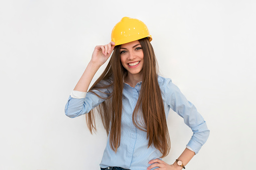 Portrait of a young female engineer with a work helmet posing on white background.