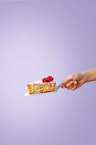 Hand holding a slice of sponge cake with berries on violet background