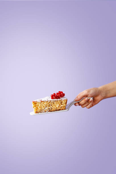 Hand holding a slice of sponge cake on violet background stock photo