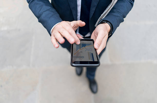 geschäftsmann mit finanz-app auf seinem handy - am telefon grafiken stock-fotos und bilder