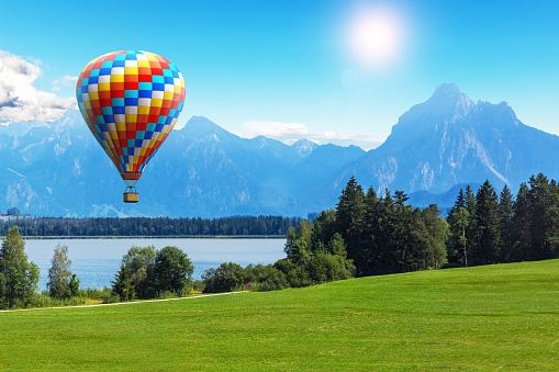 Scenic summer landscape with colorful hot air balloon flying above Alps mountains, lake and green field or meadow and forest in Bavaria, Germany, Central Europe