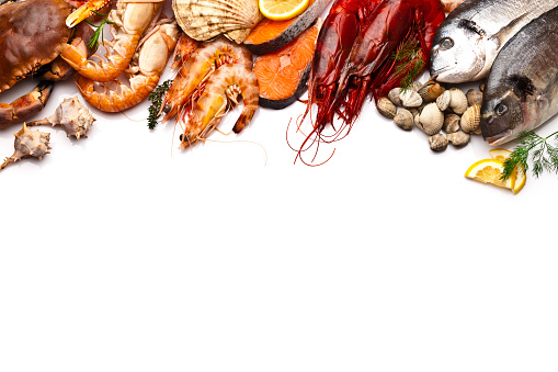 Border of different types of seafood including sea bream, mussel, crab, clams, salmon, shrimps, and prawns. Seafood is arranged at the upper border of the frame leaving a plenty copy space in the center and bottom of a white background. Colors are very vibrant and saturated. Shot directly above with DSRL Canon EOS 5D Mk II and Canon EF 70-200mm f/2.8L IS II USM Telephoto Zoom Lens