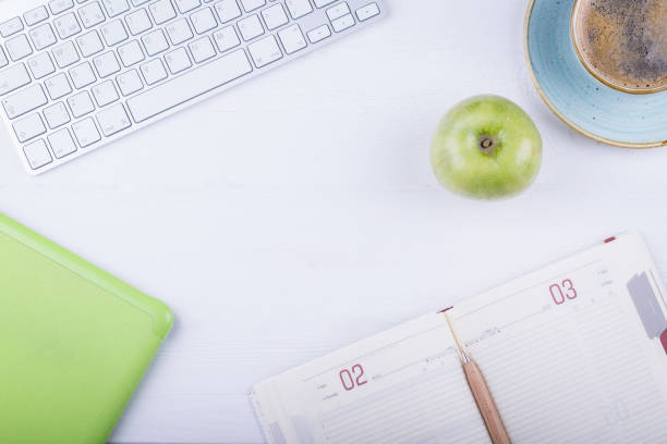 Office table with computer, notepad, mouse, pen, green apple and Office table with computer, notepad, mouse, pen, green apple and black coffee. Top view angle with copy space. apple keyboard stock pictures, royalty-free photos & images