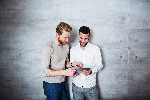 Friends standing against the wall with tablet and discussing