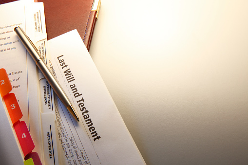 A ball point pen rests on top of an unsigned last will and testament document.  Ample room for text and copy is created by the negative space of warm gray background.