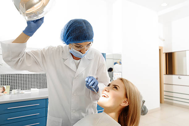 Stomatologist inspecting oral cavity of patient Dentist shining light on mouth of client to examin her fills. Clm woman looking up dental drill stock pictures, royalty-free photos & images