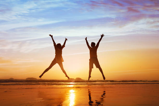 feliz pareja saltando a la playa al atardecer - jumping freedom women beach fotografías e imágenes de stock