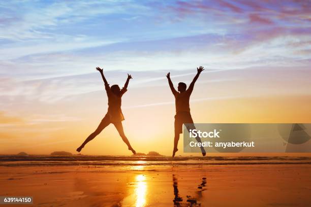 Happy Couple Jumping On The Beach At Sunset Stock Photo - Download Image Now - Healthy Lifestyle, Wellbeing, Couple - Relationship