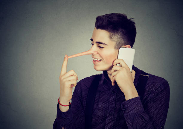 Happy man liar with long nose talking on mobile phone Happy young man with long nose talking on mobile phone isolated on gray wall background. Liar concept. Human emotion feelings, character traits falsehood stock pictures, royalty-free photos & images