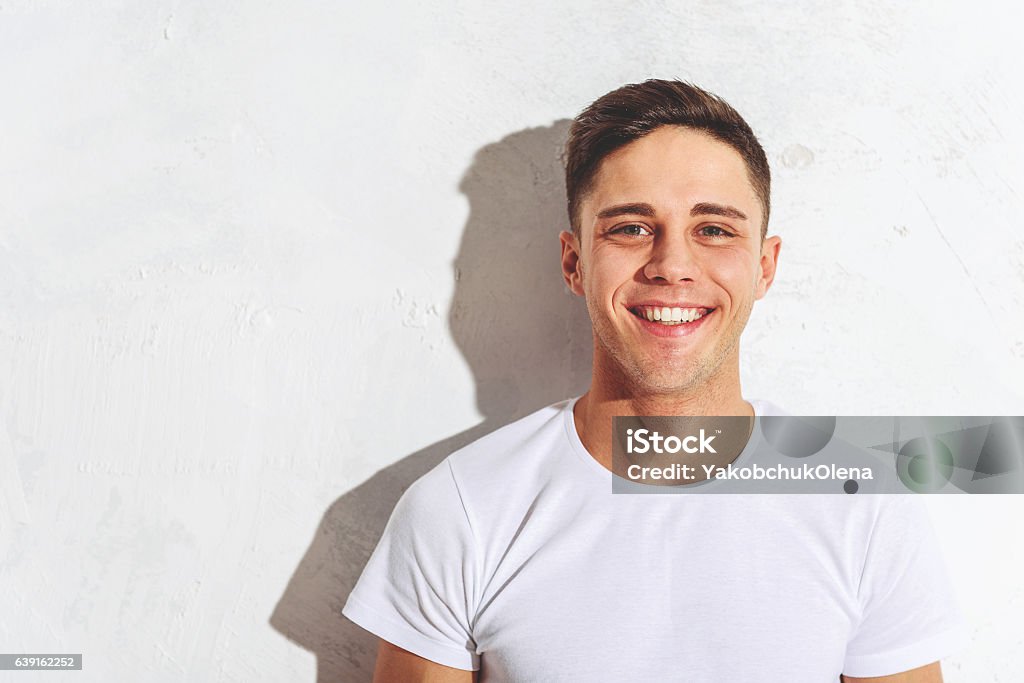 Joyful guy expressing his happiness Happy young man is standing near while wall and laughing. He is looking at camera with joy. Copy space in left side Smiling Stock Photo