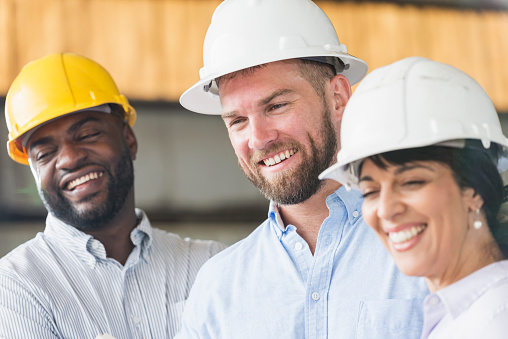 Close up of a group of multi-ethnic workers wearing hardhats. They couple be engineers, architects or construction managers. The focus is on the Caucasian man standing in the middle.