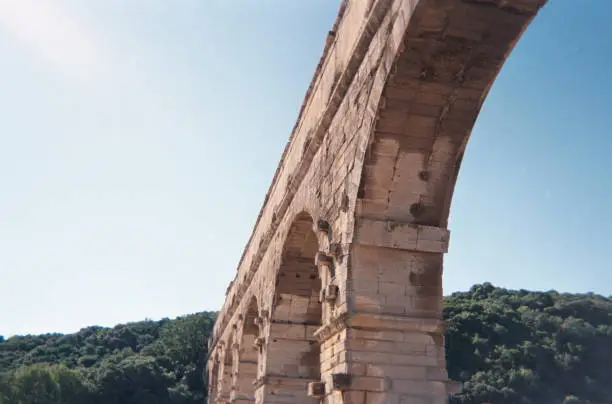 Pont du Gard is an ancient Roman aqueduct bridge built in approximately 60 A.D. outside of Nimes in modern France. This photo provides a lower, close-in angle facing up toward the hills and sky.