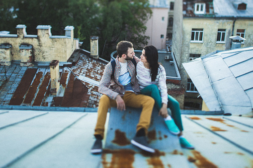 Young happy couple sitting on the roof in St. Petersburg. Beautiful view of the city from above. Casual style