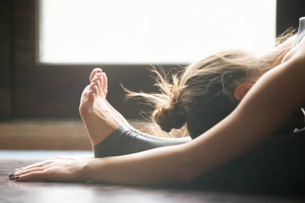 mujer joven en paschimottanasana pose, fondo interior del hogar, - leaning forward fotografías e imágenes de stock