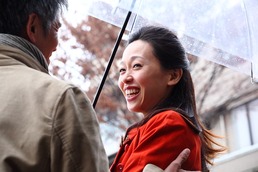 Japanese couple in one umbrella in the rain and talking happily