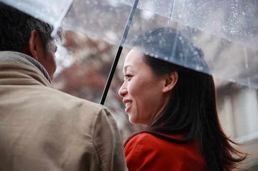 Japanese couple in one umbrella in the rain and talking happily