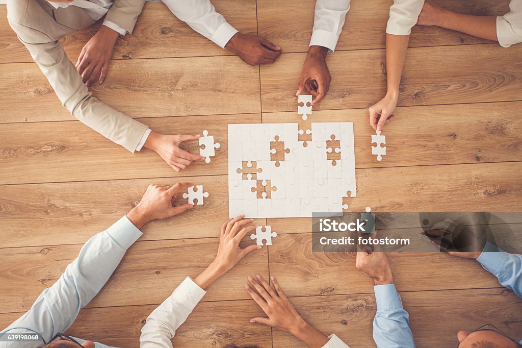 Business people finding solution together at office Business people sitting at office desk, putting puzzle pieces together, finding solution, high angle view. Puzzle Stock Photo