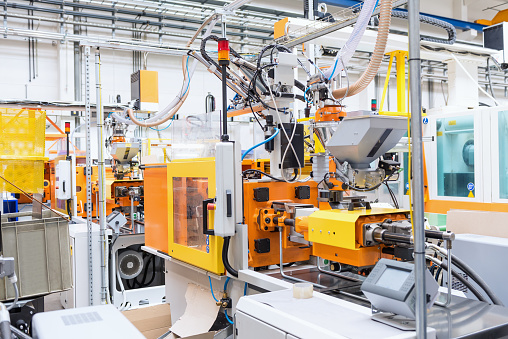 Horizontal color image of automated injection moulding machine working on plastic parts production. Powerful molding machinery in factory arranged in a row.