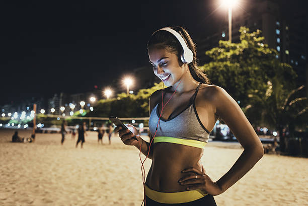 jogger using her smartphone and resting jogger using her smartphone and resting,listening music,on the beach at night teenage girls dusk city urban scene stock pictures, royalty-free photos & images