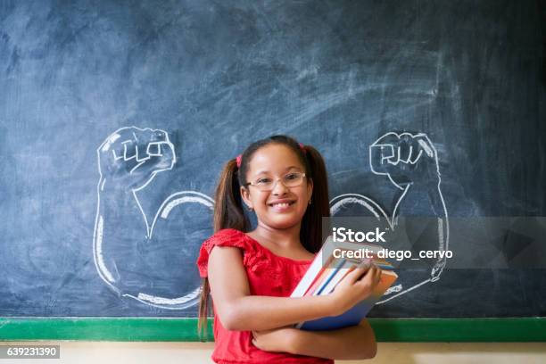 Hispanic Girl Holding Bücher Im Klassenzimmer Und Lächelnd Stockfoto und mehr Bilder von Kind