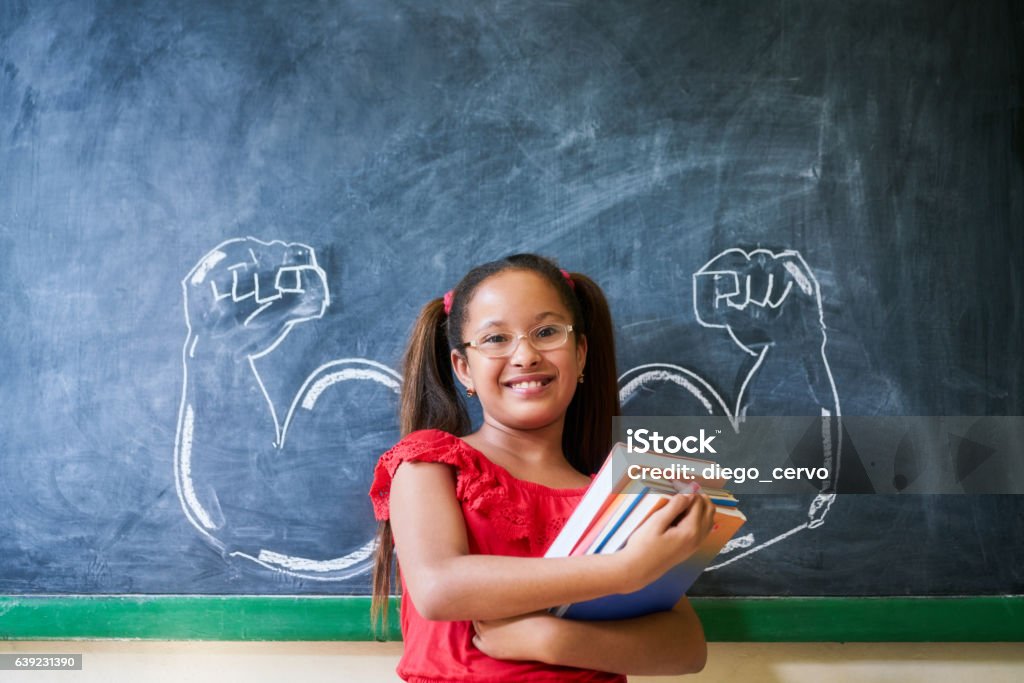 Ragazza ispanica che tiene libri in classe e sorride - Foto stock royalty-free di Bambino