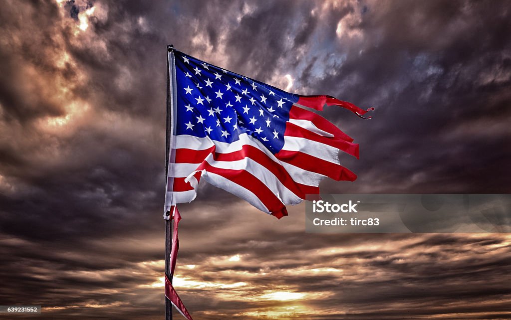 Tattered American flag flapping in ominous sky Torn Stock Photo