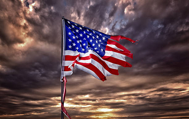 Tattered American flag flapping in ominous sky Tattered American flag flapping in ominous sky run down stock pictures, royalty-free photos & images