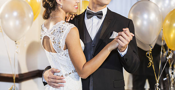 Cropped teenage couple at prom dancing A cropped view of a teenage couple at the prom dancing a slow dance. The mixed race girl is smiling, wearing an elegant white dress. Her date is wearing a tuxedo. prom stock pictures, royalty-free photos & images